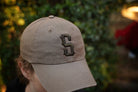 Beige cap with a logo worn by a person against a blurred green background