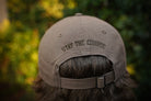 Beige cap with 'Stay the Course' text worn by a person against a blurred green background