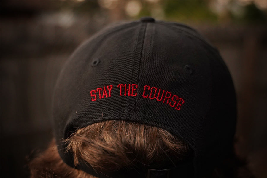 Black cap with 'Stay the Course' text worn by a person, blurred background