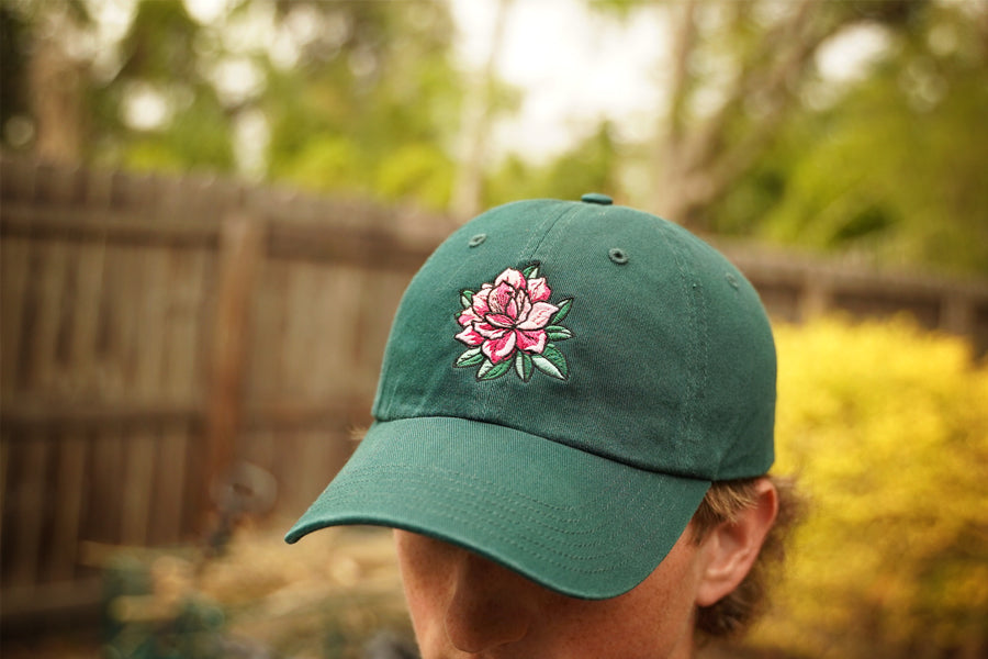 Green cap with a pink floral design worn by a person outdoors.