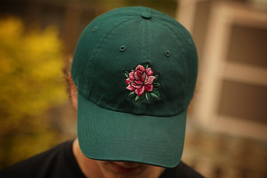 Green cap with a pink azalea embroidery on a blurred background