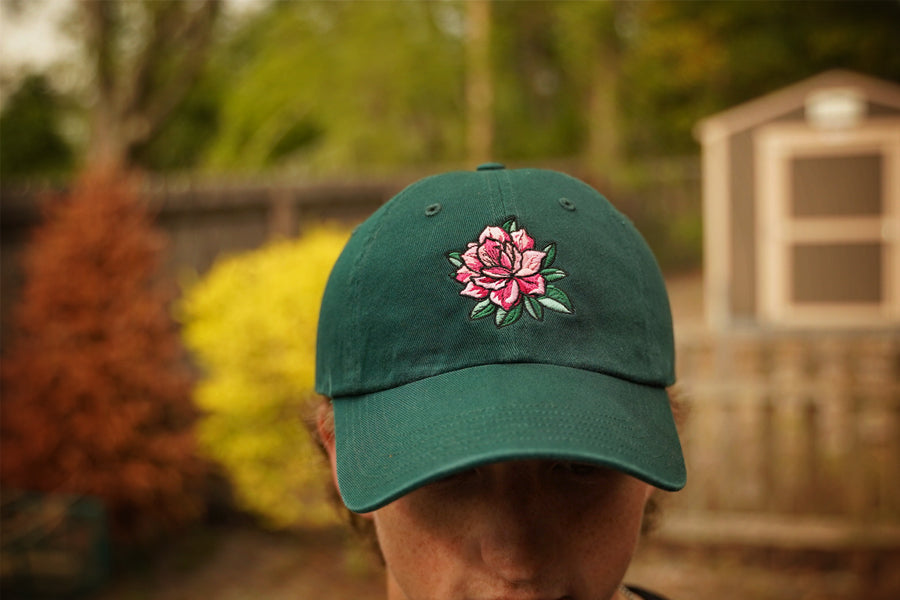 Green cap with a pink flower design worn by a person outdoors.
