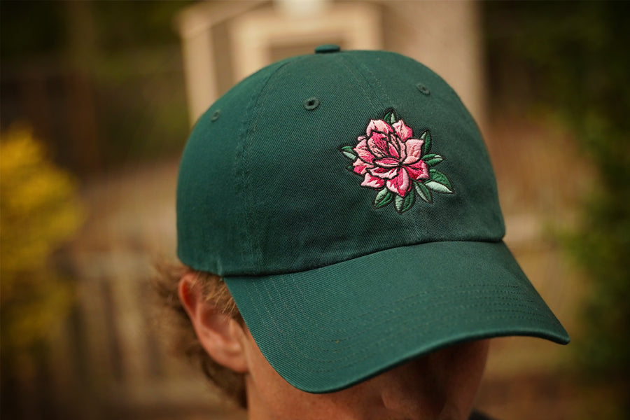 Green cap with a pink flower design worn by a person outdoors.