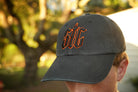 Person wearing a black hat with orange and black "stc" puff embroidery on the front, in an outdoor setting