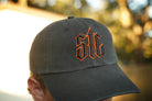 Person wearing a black hat with orange and black "stc" puff embroidery on the front, in an outdoor setting