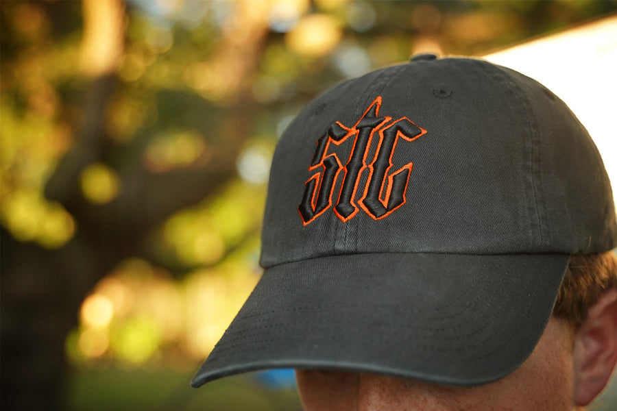 Person wearing a black hat with orange and black "stc" puff embroidery on the front, in an outdoor setting