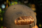 Person wearing a black hat with  black "stay the course" embroidery on the back, in an outdoor setting