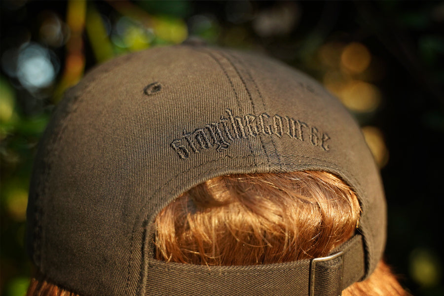 Person wearing a black hat with  black "stay the course" embroidery on the back, in an outdoor setting