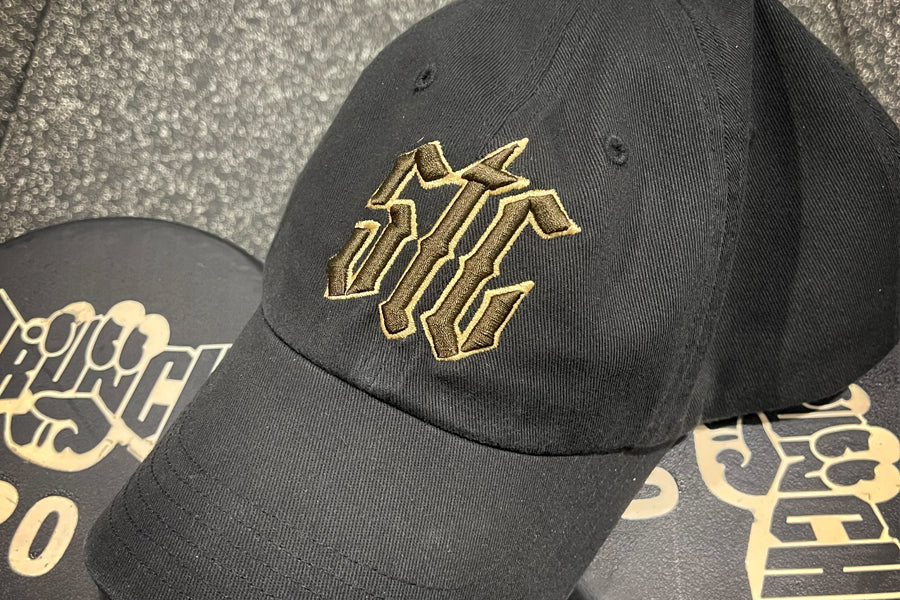 Black cap with gold and brown logo on a textured surface