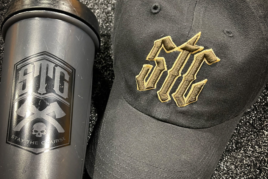 Black tumbler and black cap with gold and brown logo on a textured surface