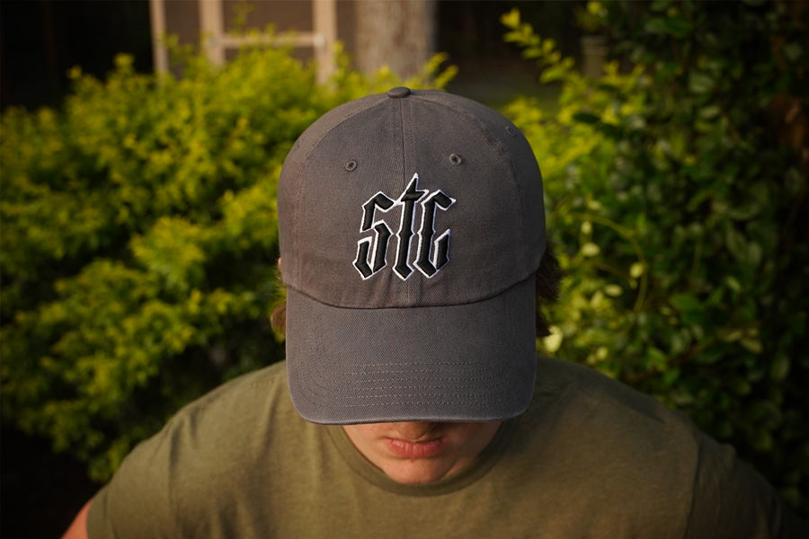 Person wearing a gray cap with 'STC' logo in front of green foliage