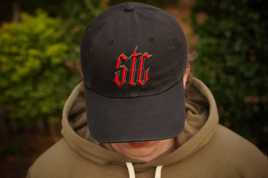 Person wearing a black cap with red and green logo, blurred green background