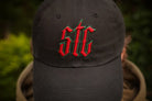 Black cap with red and green logo worn by a person against a blurred natural background