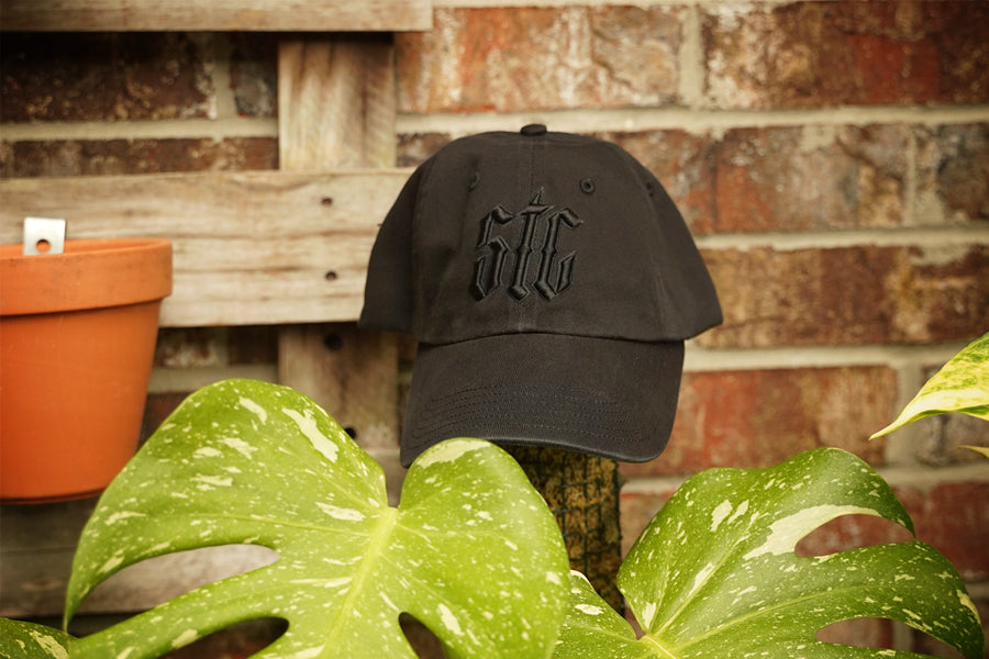 Black cap with 'STC' logo on a wooden post with plants and a brick wall in the background