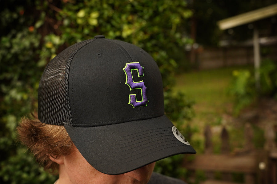 Person wearing a black cap with a purple logo outdoors