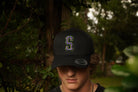 Person wearing a black cap with a 'S' logo in a forest setting