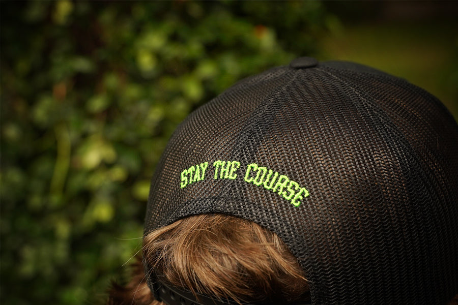 Person wearing a cap with 'Stay the Course' text against a blurred green background
