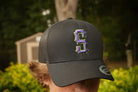 Person wearing a black cap with a purple and green logo outdoors