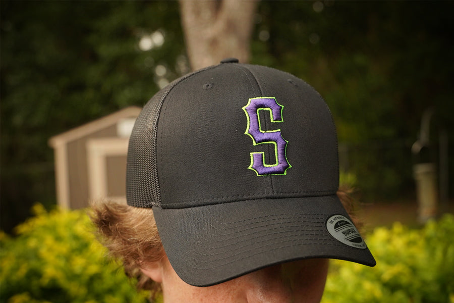 Person wearing a black cap with a purple and green logo outdoors