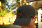 Person wearing a black hat with orange and black "s" puff embroidery on the front, in an outdoor setting
