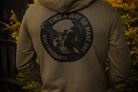 Person wearing a hoodie with a skull design and text on the back, standing in front of blurred greenery.