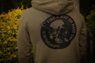 Person wearing a green hoodie with a skull and crossbones design on the back, featuring text.