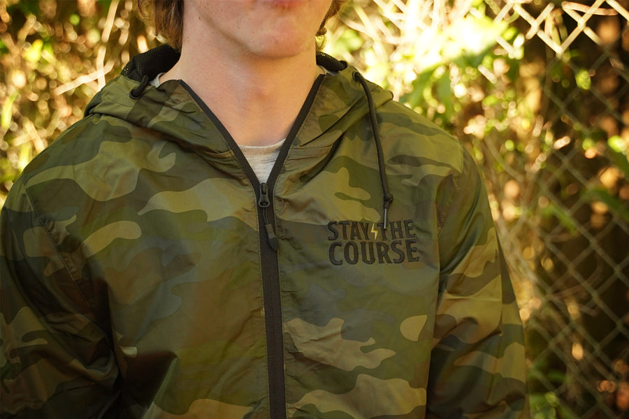 Person wearing a green camouflage jacket with 'Stay the Course' text, outdoors.