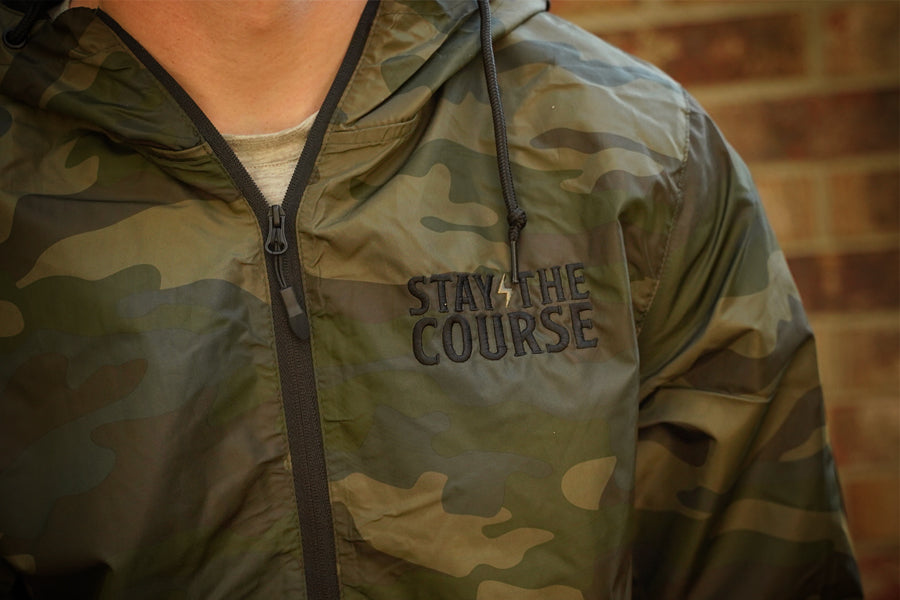 Camouflage jacket with 'Stay the Course' text on a brick wall background
