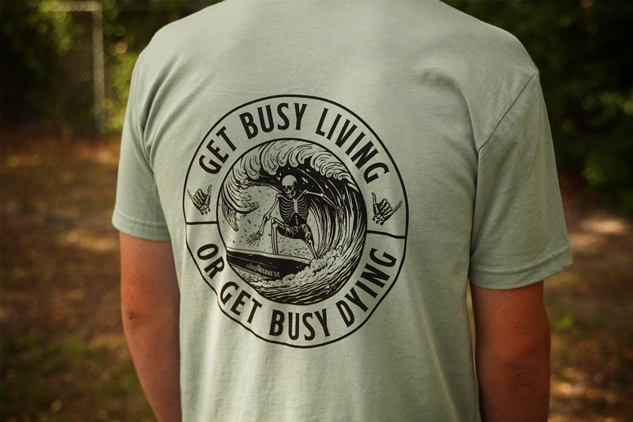 Person wearing a green shirt with black graphic that says "get busy living or get busy dying"