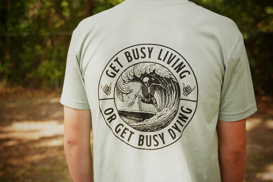 Person wearing a green shirt with black graphic that says "get busy living or get busy dying"