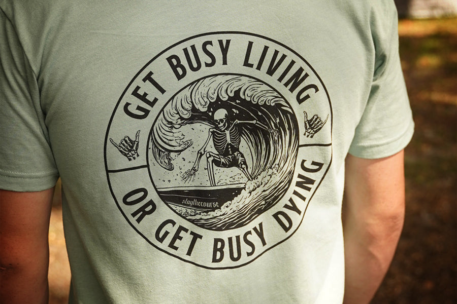 Person wearing a green shirt with black graphic that says "get busy living or get busy dying"