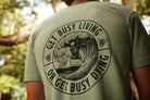 Person wearing a green shirt with black graphic that says "get busy living or get busy dying"