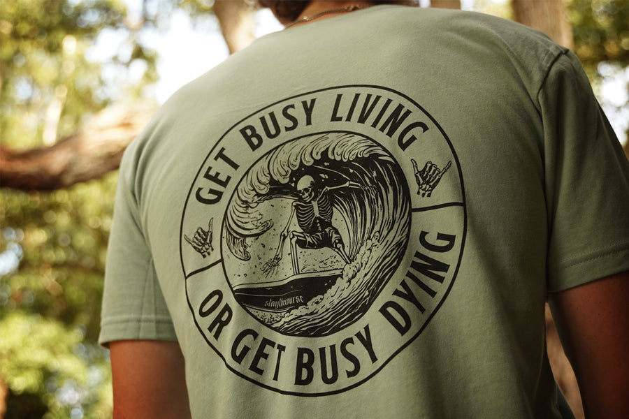 Person wearing a green shirt with black graphic that says "get busy living or get busy dying"