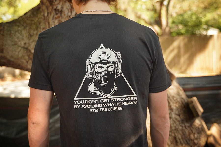 Person wearing a black t-shirt with a graphic design and text on the back, standing outdoors.