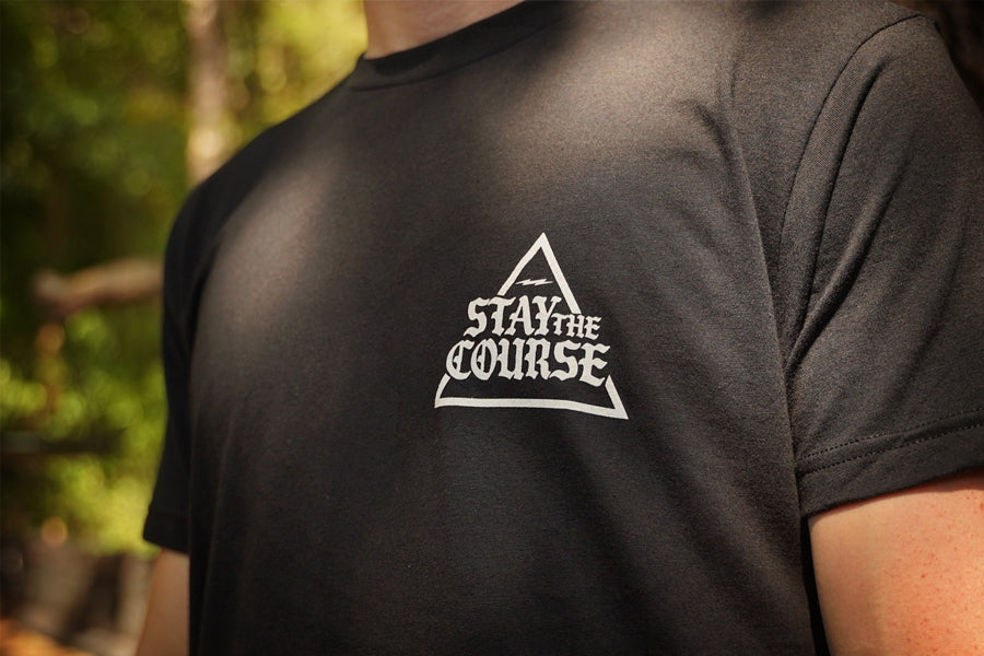 Person wearing a black t-shirt with 'Stay the Course' logo outdoors