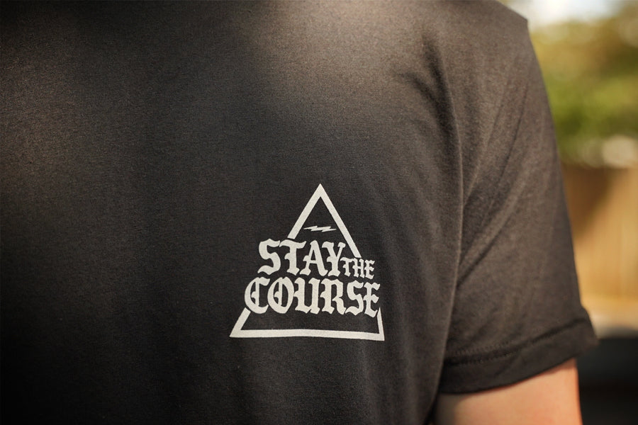 Black t-shirt with 'Stay the Course' triangle logo on the back, blurred background