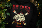Black hoodie with 'Give 'em Hell' and graphic design on a person standing among greenery