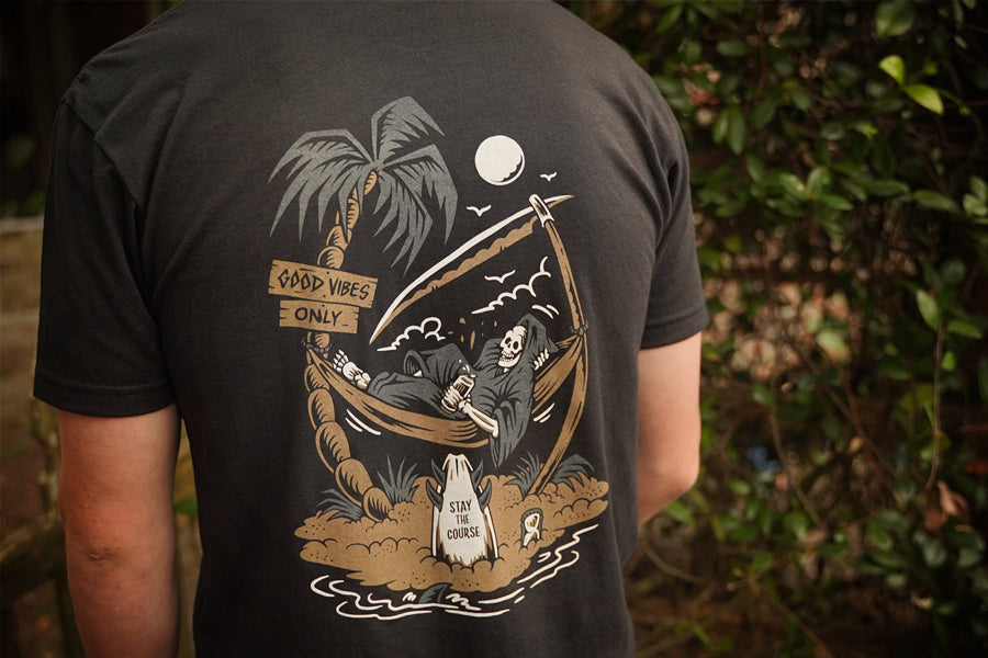 Person wearing a black t-shirt with a graphic design on the back, featuring a reaper and palm trees.