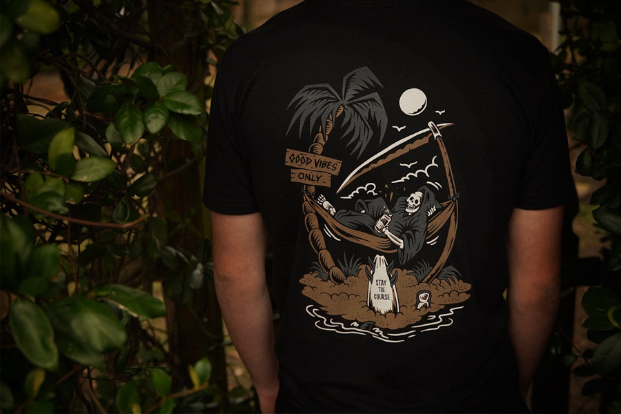 Person wearing a black t-shirt with a graphic design of a reaper chilling in a hammock, and palm trees on a dark background.