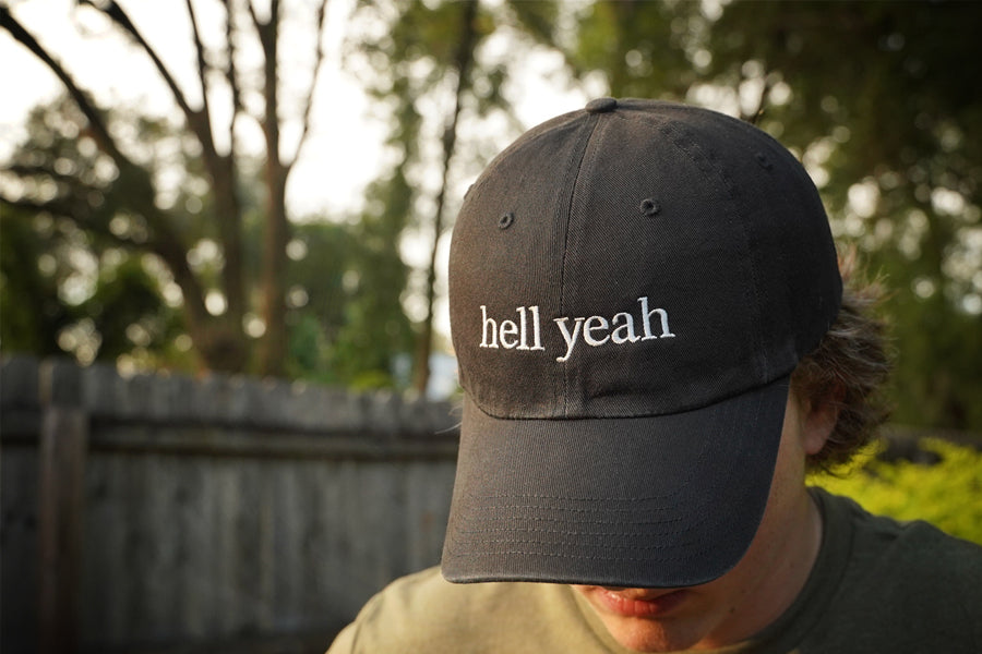 Person wearing a black cap with 'hell yeah' text outdoors