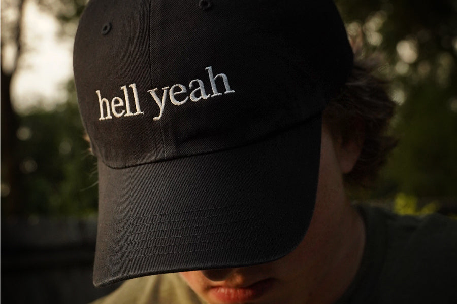 Black cap with 'hell yeah' text worn by a person outdoors