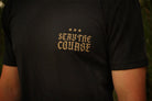 A close-up of a person wearing a black t-shirt with a gold printed graphic on the chest that reads 'STAY THE COURSE' with three stars above it.