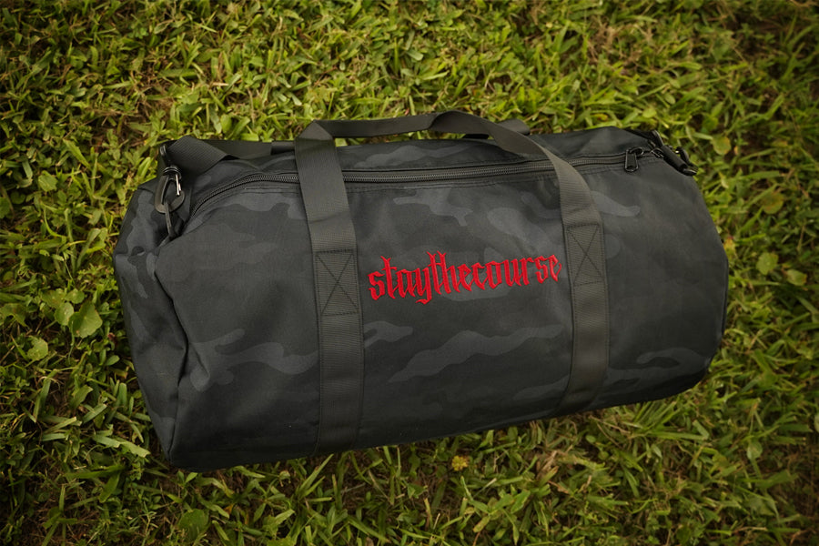 black camo duffle bag with red embroidery in grass