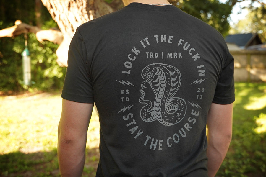 Person wearing a black t-shirt with a snake graphic and text outdoors