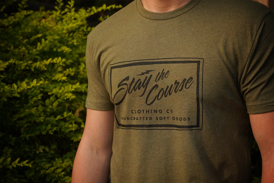 Person wearing a green t-shirt with 'Stay the Course' branding outdoors.