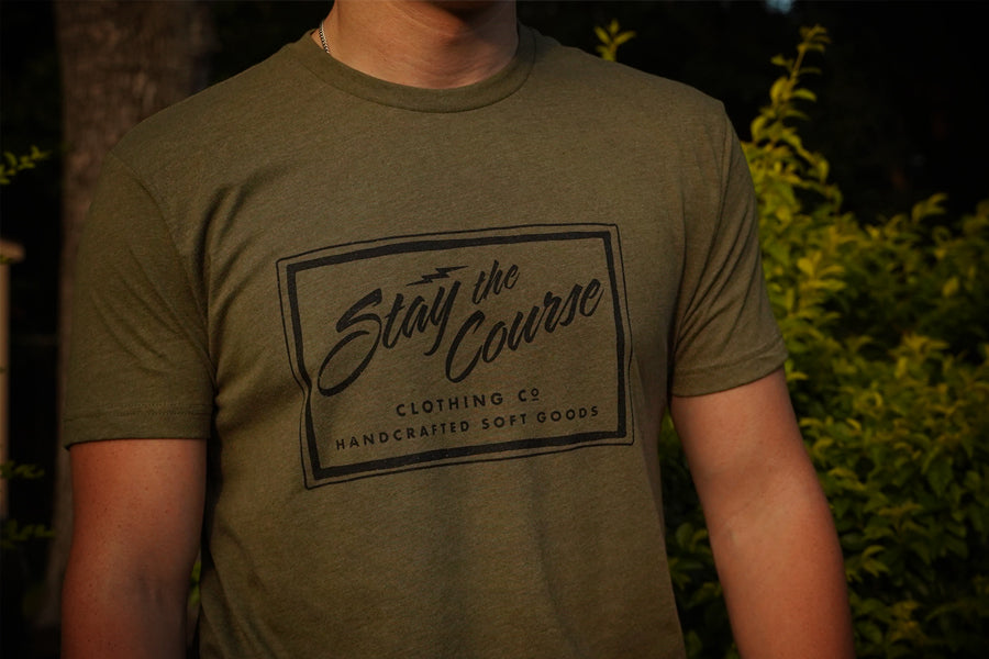 Person wearing a green t-shirt with 'Stay the Course' branding outdoors.