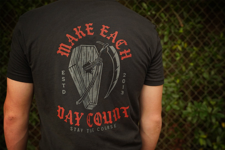 Black t-shirt with red and gray graphic and text on a person against a blurred background