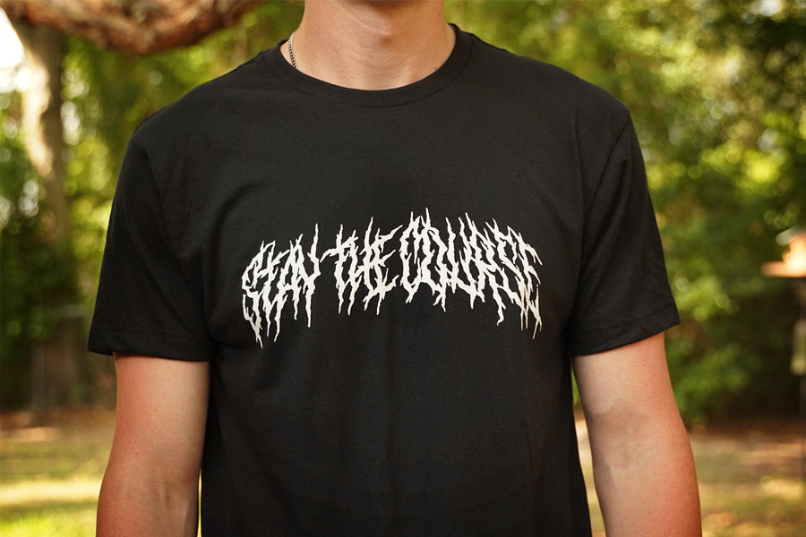 Person wearing a black T-shirt with "Stay the Course" printed in white in heavy metal style