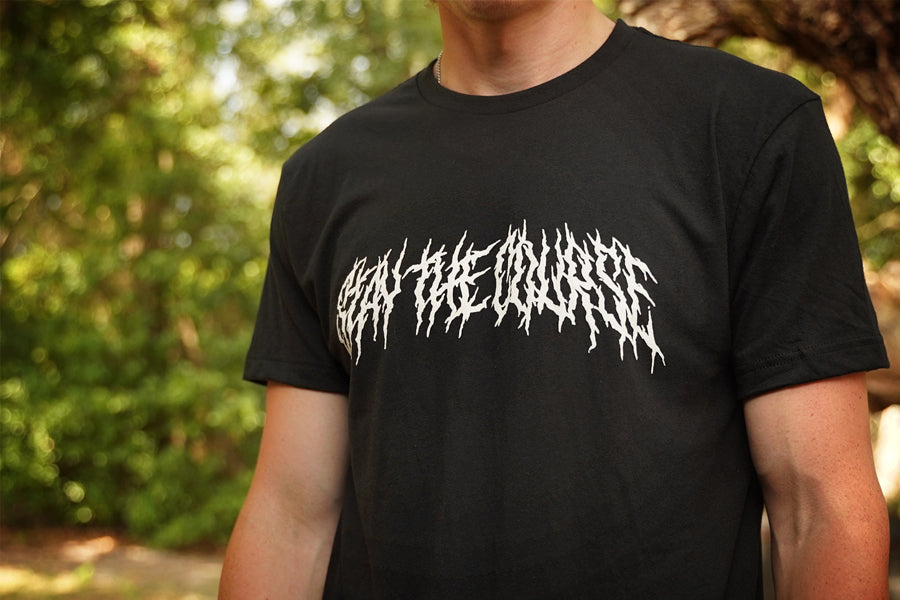 Person wearing a black T-shirt with "Stay the Course" printed in white in heavy metal style