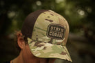Camouflage cap with 'Stay the Course' logo worn by a person outdoors